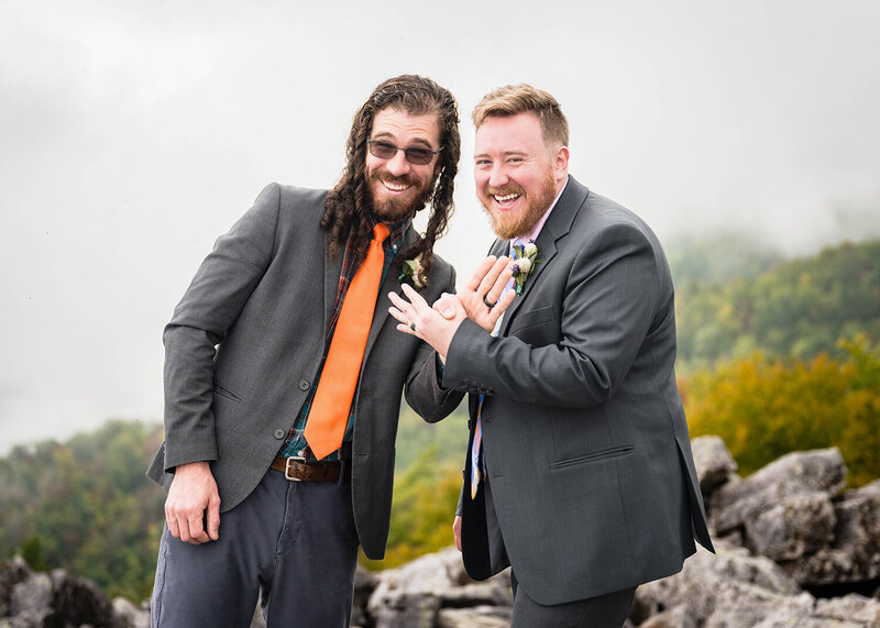 A queer couple stand on rocks during their elopement ceremony in Shenandoah National Park and smile for a photo during their ring exchange.
