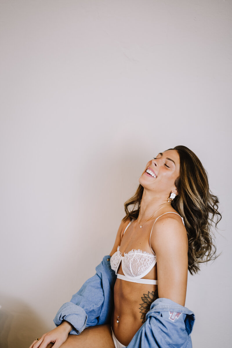 A women smiling in a white bra with jean jacket.