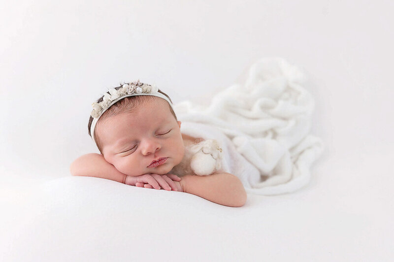 newborn girl on a white backdrop with a white wrap on her.  She is holding a tiny lamb for her newborn photography session in Burlington, Ontario