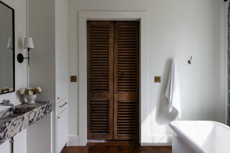 Vintage French doors are the focal point for this European inspired primary bathroom.