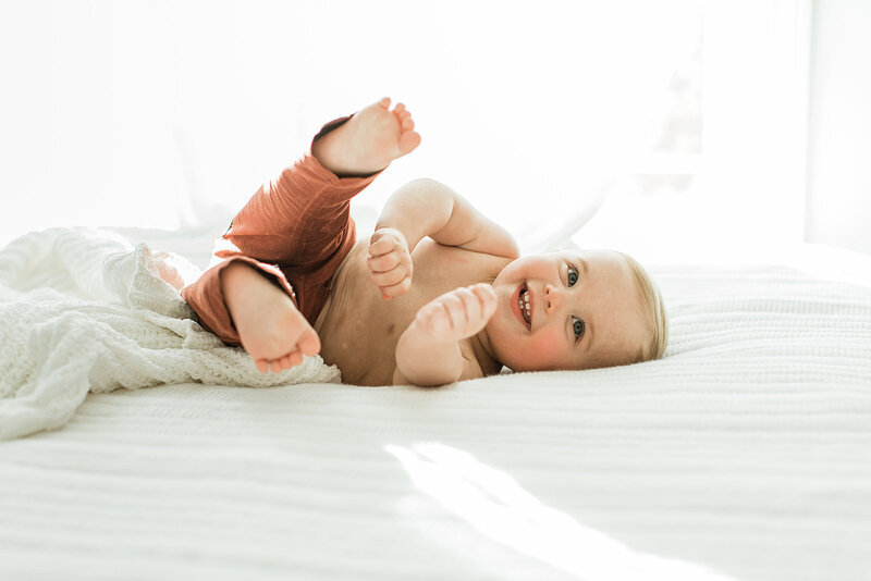 6 month old baby finds his feet and rolls around on bed near window