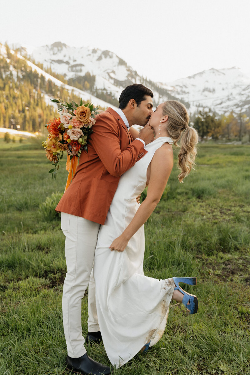 Picture of a bride and groom kissing in a field taken by an elopement photographer with trees in the background