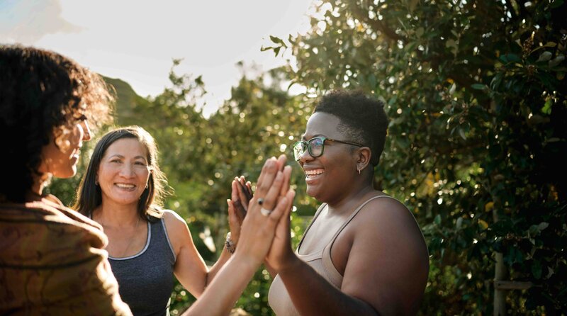 Three women connecting during a heart-centered equine assisted group session in nature