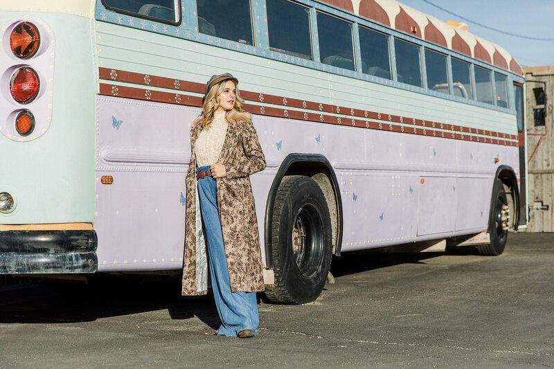 Retro-inspired teen model in flared jeans, a vintage coat, and a beret standing next to a pastel-colored vintage bus – captured at a photography workshop.