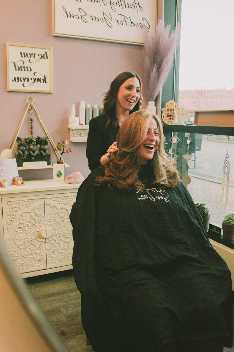 Hairstylist laughing with a client in her chair at Art & Soul Hair Studio in New York