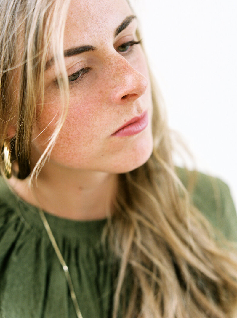 Woman in green blouse brushes hair out of face and looks into the distance