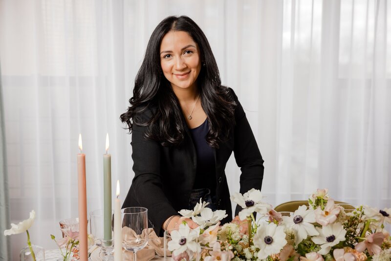 Portrait of Kathiya, Zela Events wedding planner styling a table with elegant floral arrangements and candles, smiling warmly at the camera.