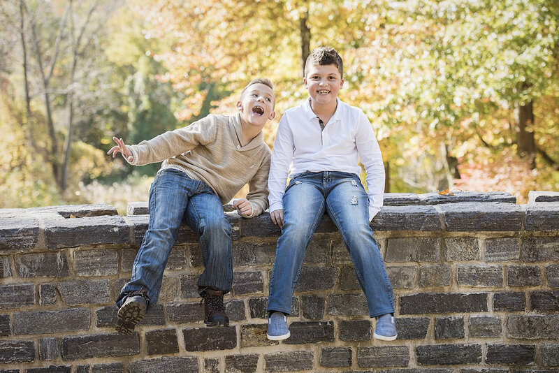 Two kids smiling and sitting on the top of a brick wall