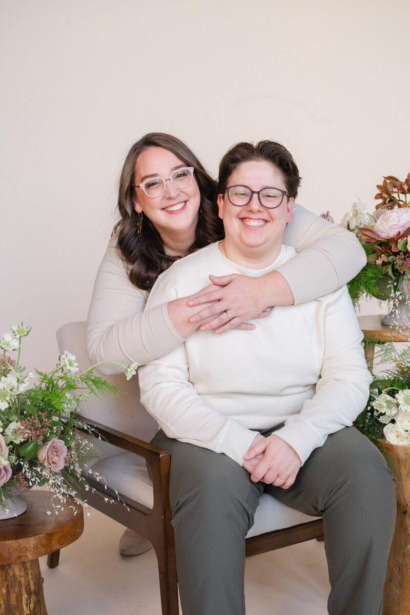 A person sitting behind their partner with their arms around them as they both smile