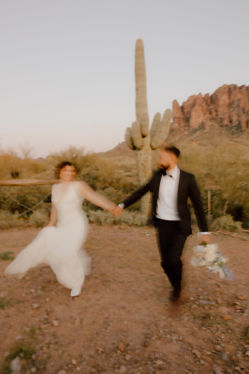 bride and groom running through the desert holding hands