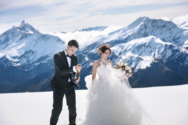 A bride and groom popping champagne on a snowy mountaintop.
