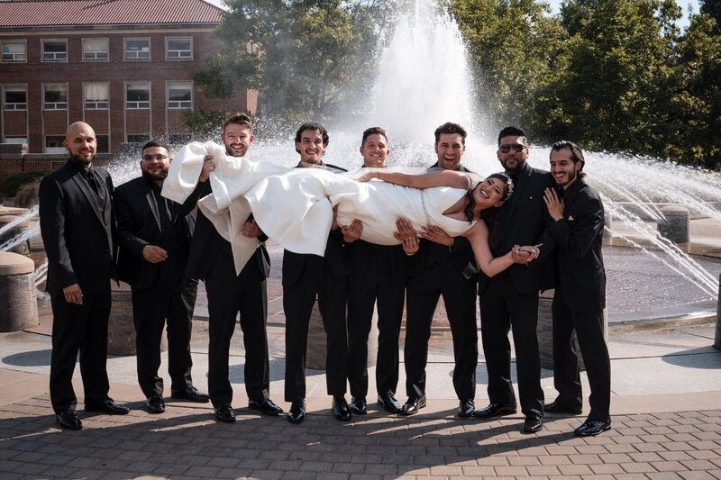 Groomsmen lift the bride in front of fountain at Union Club Hotel