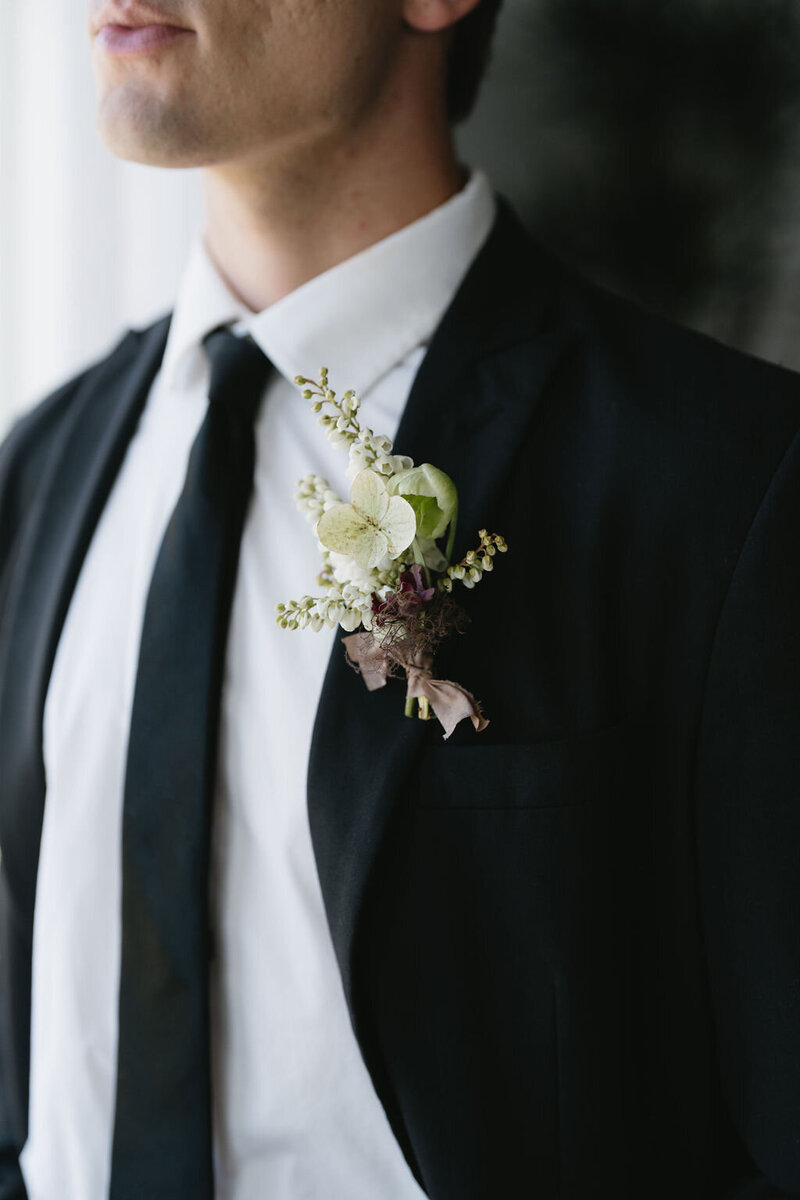 Groom's elegant, green and plum, boutonniere on a white button down and black suit with black tie
