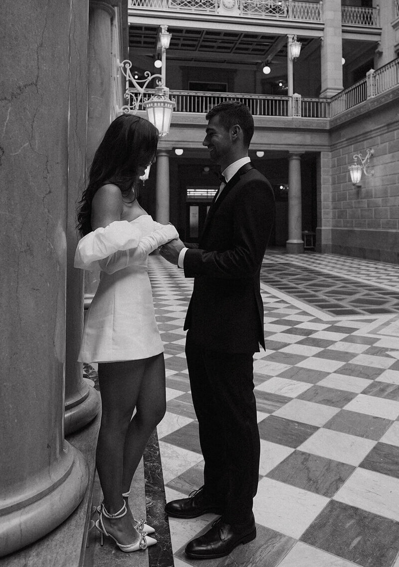 The groom and bride are smiling and looking at each other while standing. at the City Hall