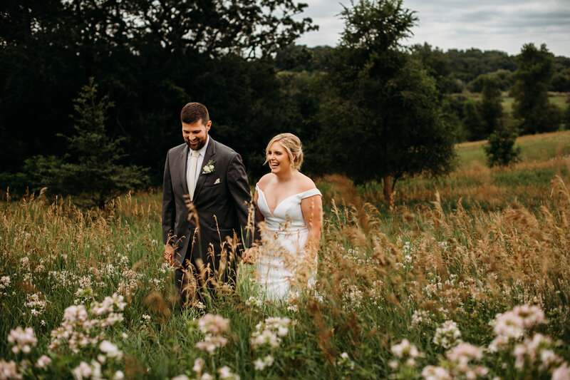 Bride and groom walking through field of wild flowers