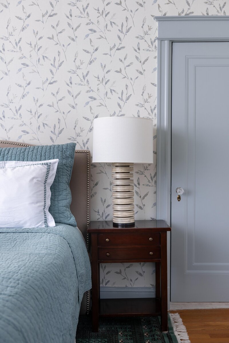 Bedroom featuring patterned wallpaper, a comfortable bed with white bedding, a modern lamp on the bedside table, and decorative pillows