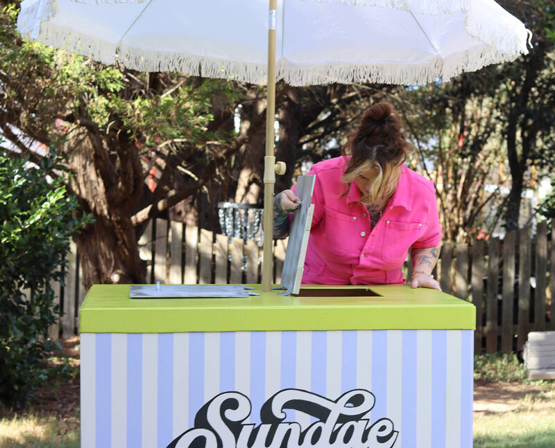 A woman looking into the compartment of a striped ice-cream cart.