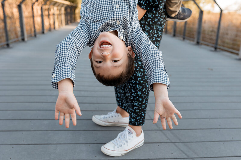 Family Photographer, A littl boy hangs upside down smiling outside