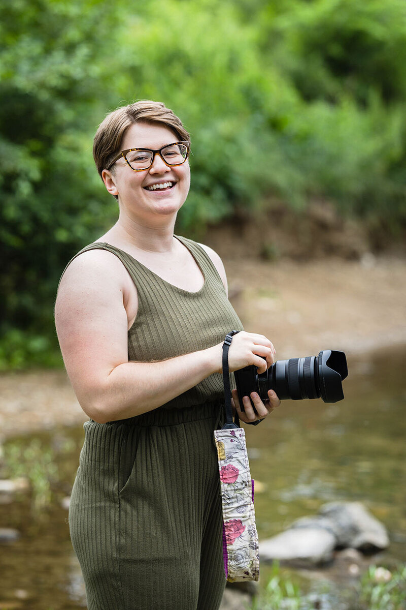 A Virginia elopement photographer holds her camera and smiles towards the camera.