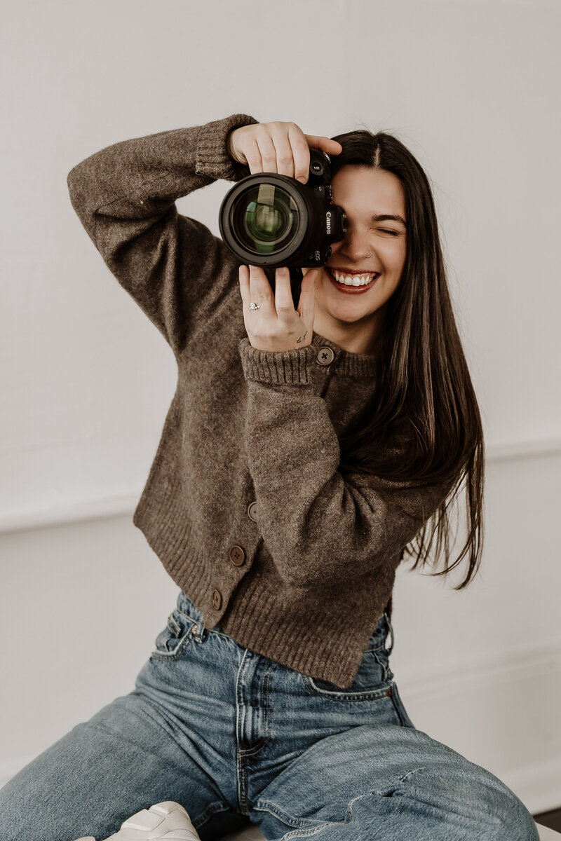 Professional female photographer peering through camera during branding session in natural light studio – Bedminster, NJ