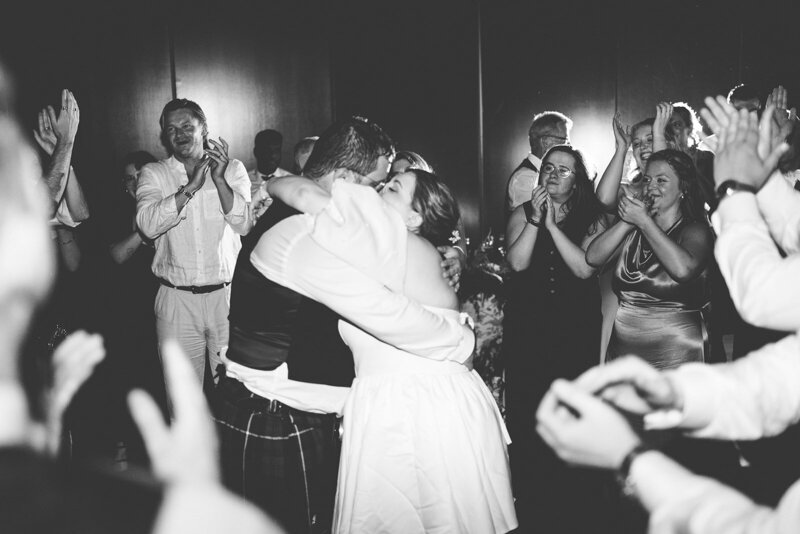 Black and white image of the bride and groom holding on another on the dance floor surrounded by wedding guests dancing in the ballroom at District Winery in DC 