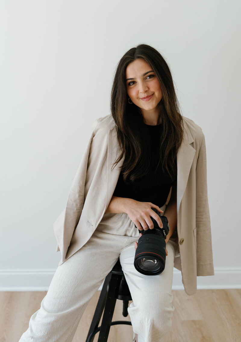 Reilly Erin, a wedding photographer based in Fort Worth, Texas, sitting on a stool with her camera in hand.