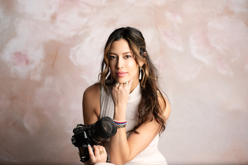 Photographer, Drea Schod, posing for headshot with hand under chin holding camera in other hand