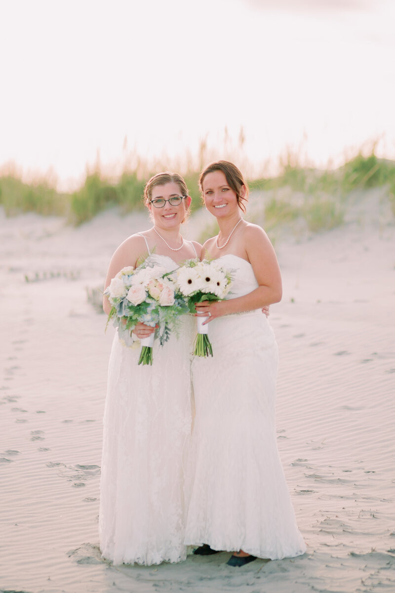 Newlyweds hold flowers and each other on the beach.