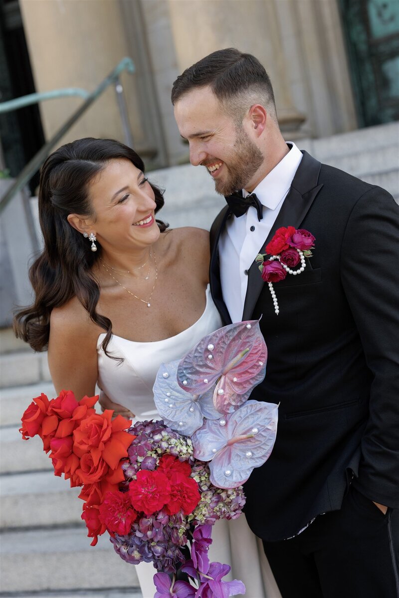 bride and groom holding one another laughing with the bride holding a vibrant modern bouquet