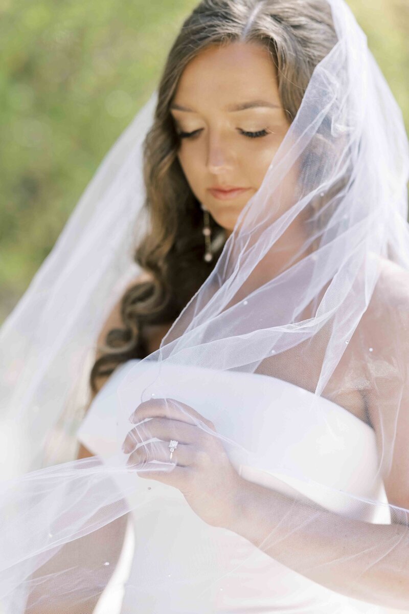 bride in a wedding dress looking down at her veil