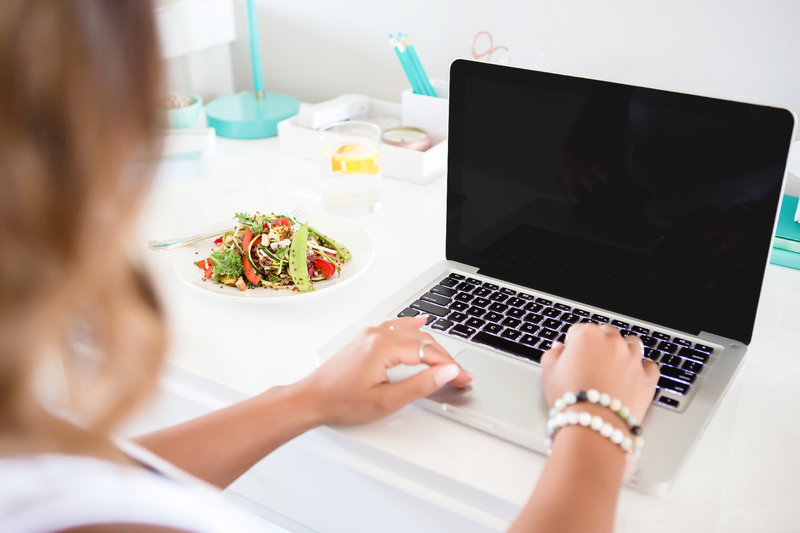 Healthy lunch with avocado and salad next to a woman working on a laptop in a modern, bright workspace. 