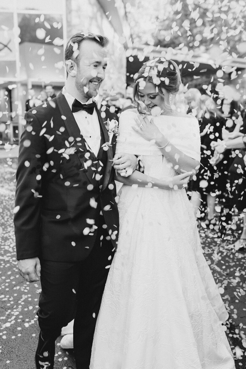 Black and white photo of bride and groom being showered with confetti