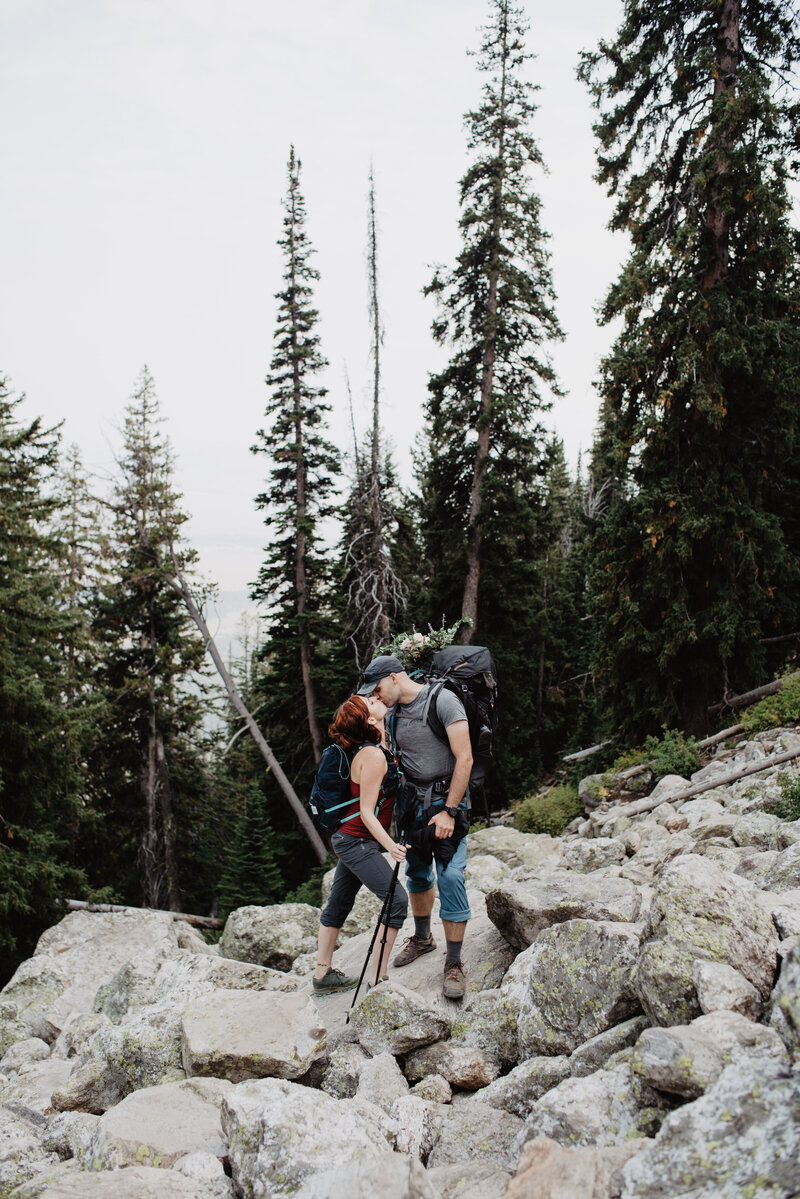 delta lake hike with man and woman kissing as they hike large rocks with tall pines in the distance for a grand teton wedding
