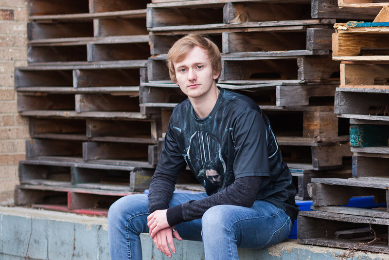 st thomas aqauanis high school senior guy sitting on concrete ledge with pallets stacked behind him, photographed in Hartville Ohio, photographed by Jamie Lynette Photography Canton Ohio Senior Photographer