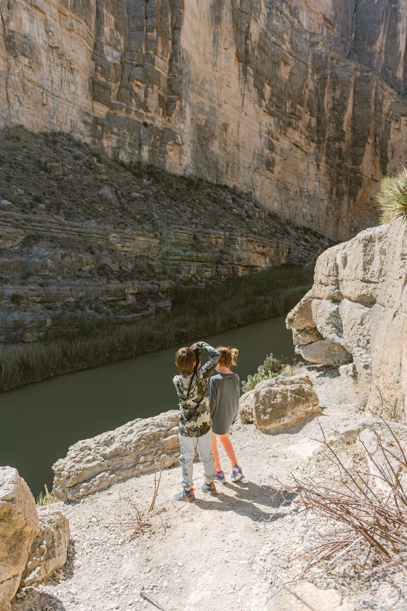 Color photograph of a mother and three children standing at the edge of a canyon in Big Bend, Texas. Editorial, luxury family imagery captured by Erin Marcin Photography, highlighting natural textures, high-end storytelling, and organic light in a dramatic desert landscape.