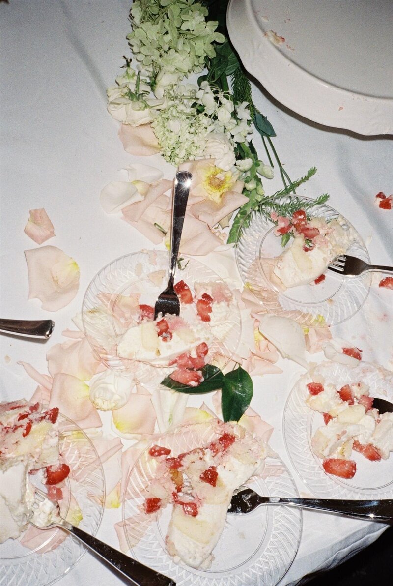 A group of wedding cake slices on plates with strawberries on a white linen