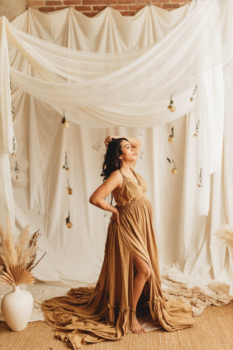 pregnant mother standing in front of a white draped backdrop with hanging dried flowers