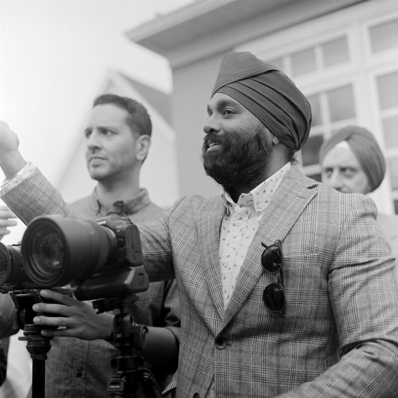 Sikh photographer in a suit directing his client with a camera on a tripod