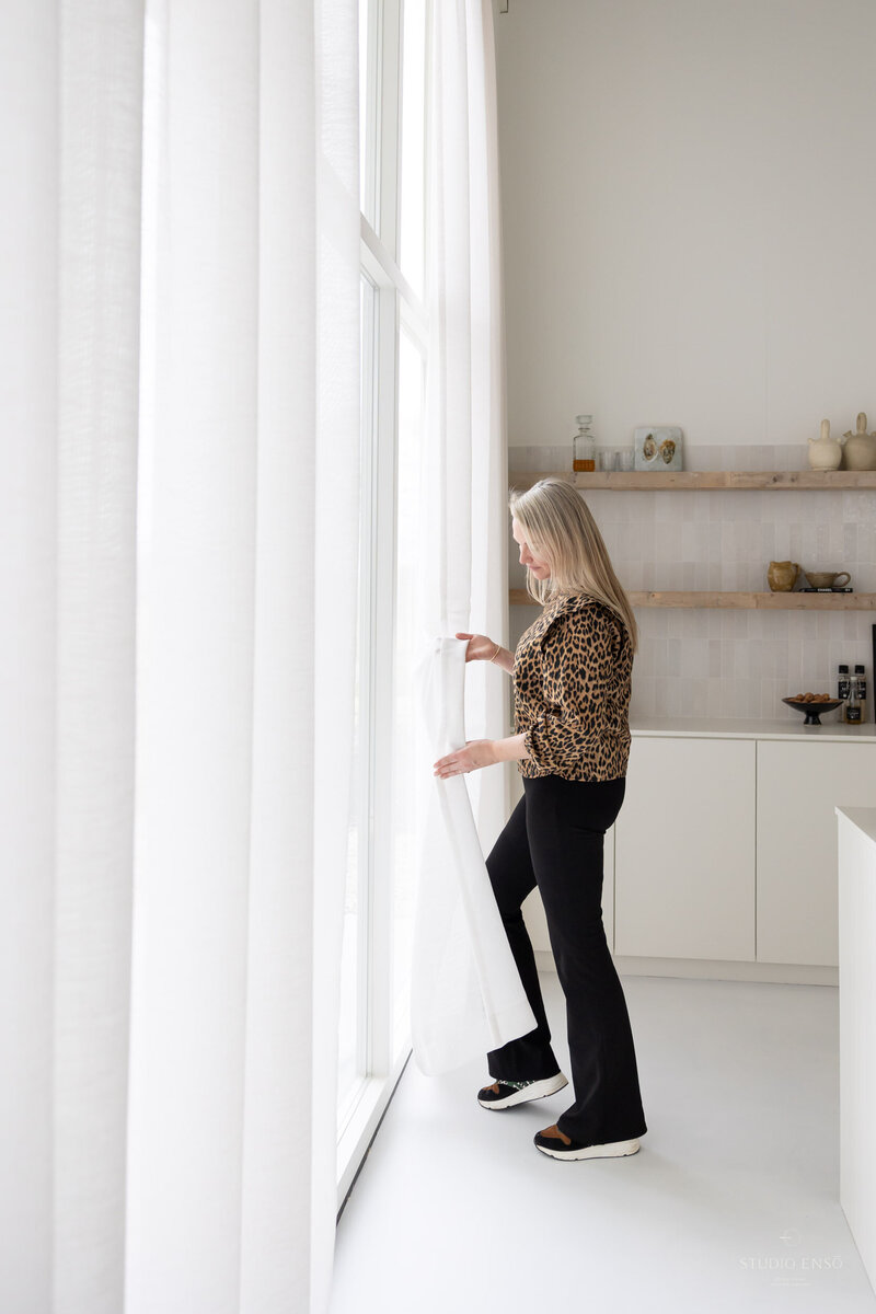 interieurontwerper Eline in een strakke witte keuken met gietvloer en linnen gordijnen