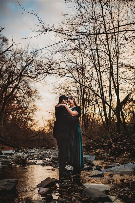 Maryland wedding photographer captures engagement session with man and woman embracing one another while standing in a rocky stream in the woods