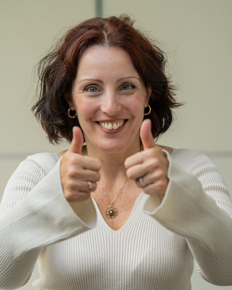 Csilla close up with a smile, giving a thumbs up with both hands.