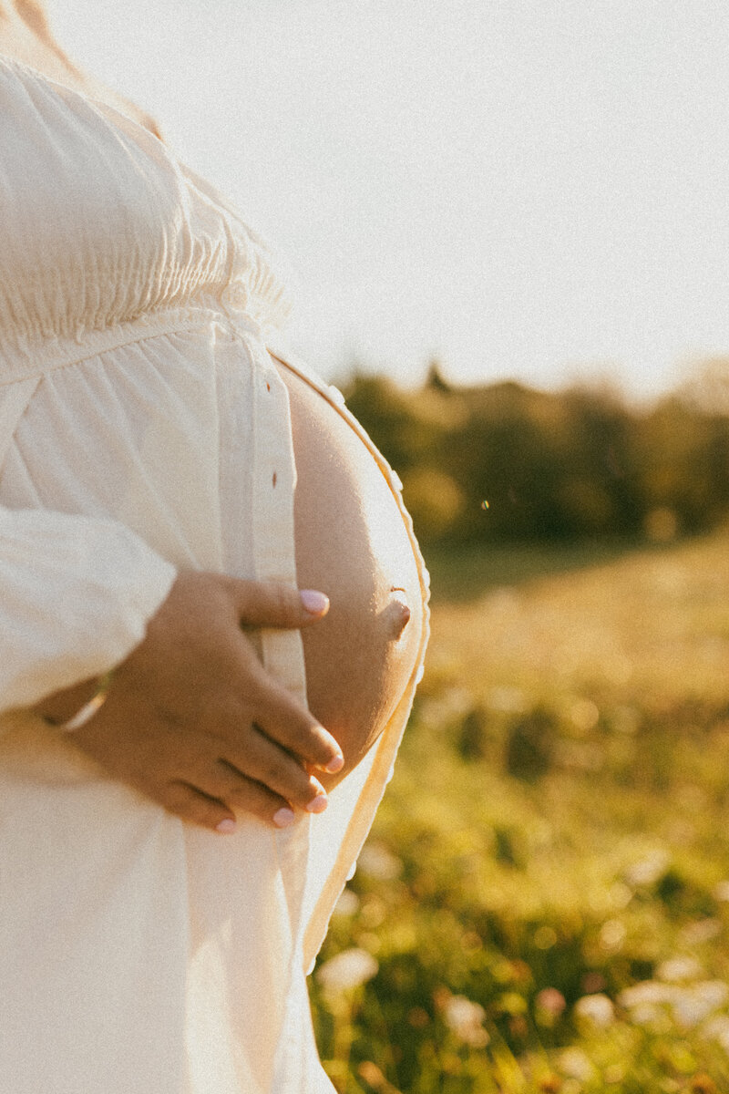 A mother wearing a maternity dress from lucy janes client wardrobe during a sunset maternity photoshoot in christchurch