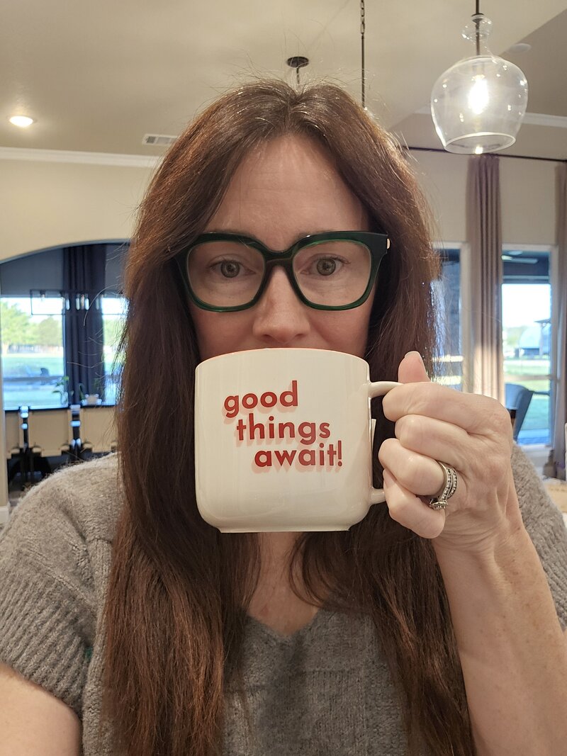 Trish drinking tea from a mug with 'good things await' written on it