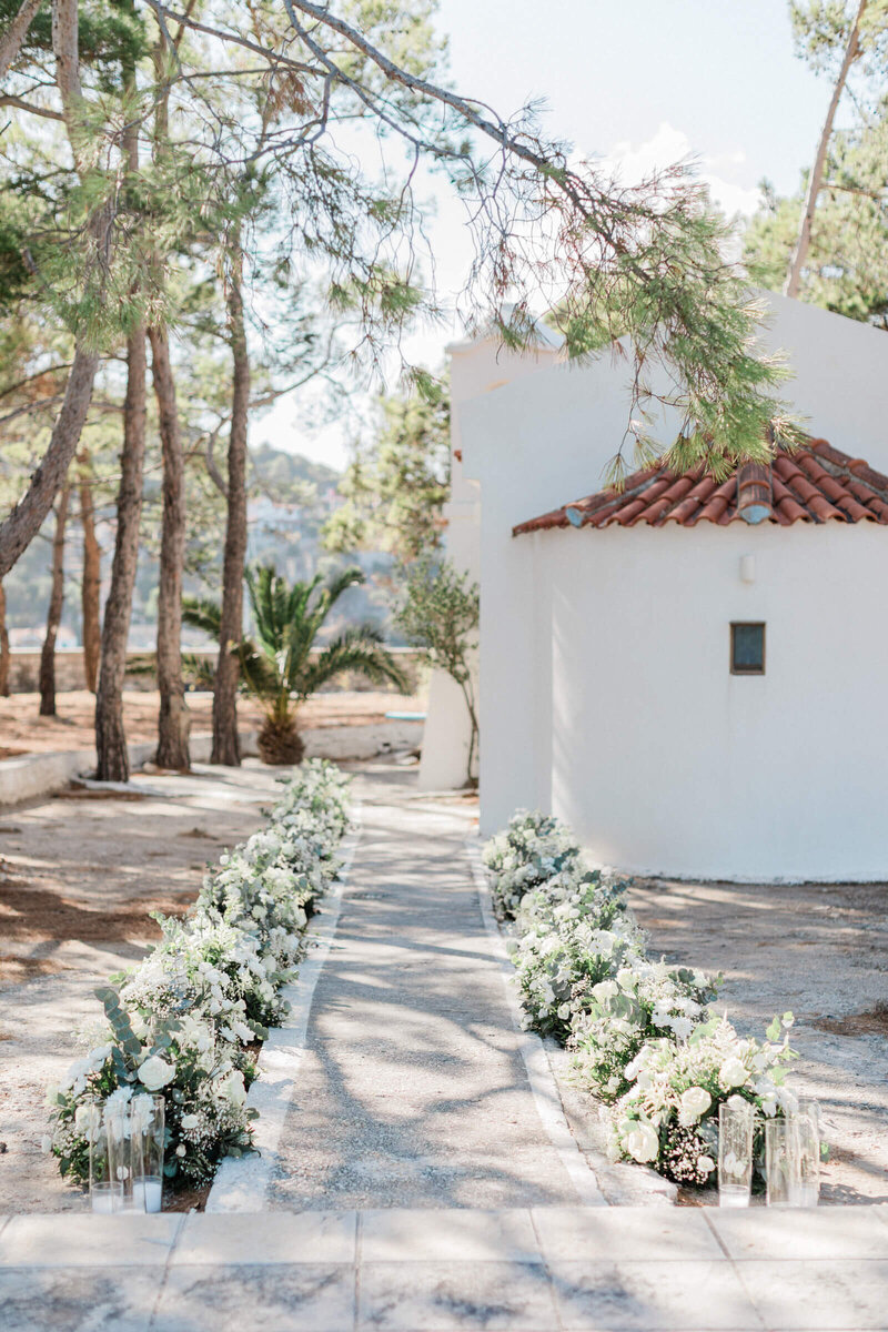 Floral aisle decor outside a white chapel, designed by an Ionian Islands wedding planner for a romantic destination celebration.