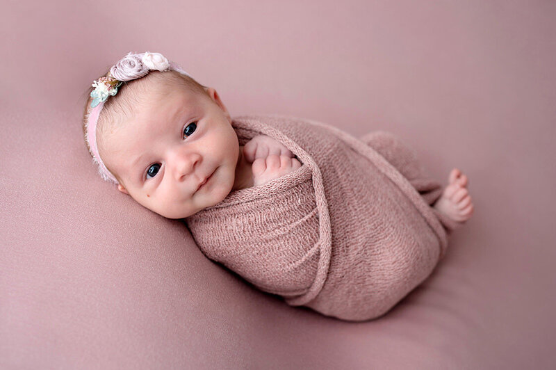 Swaddled baby girl smiling at the camera during newborn photo session.