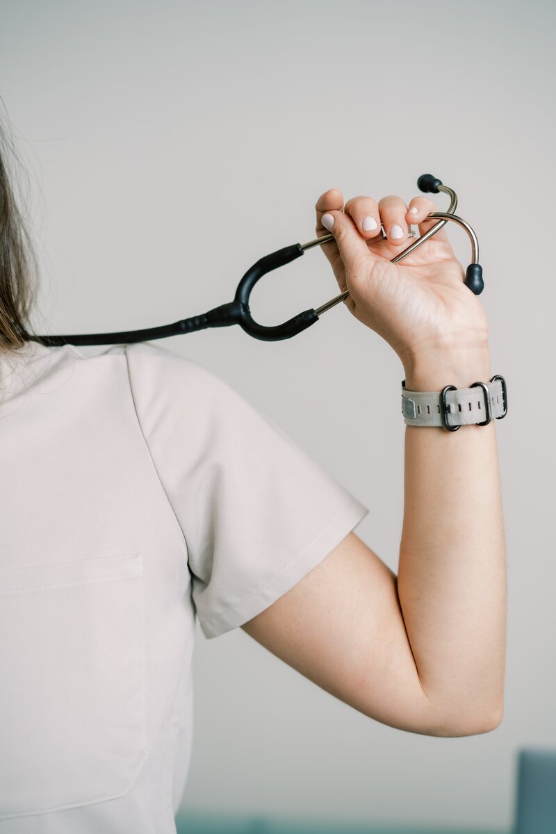 Nurse wearing tan scrubs holding up a stethoscope