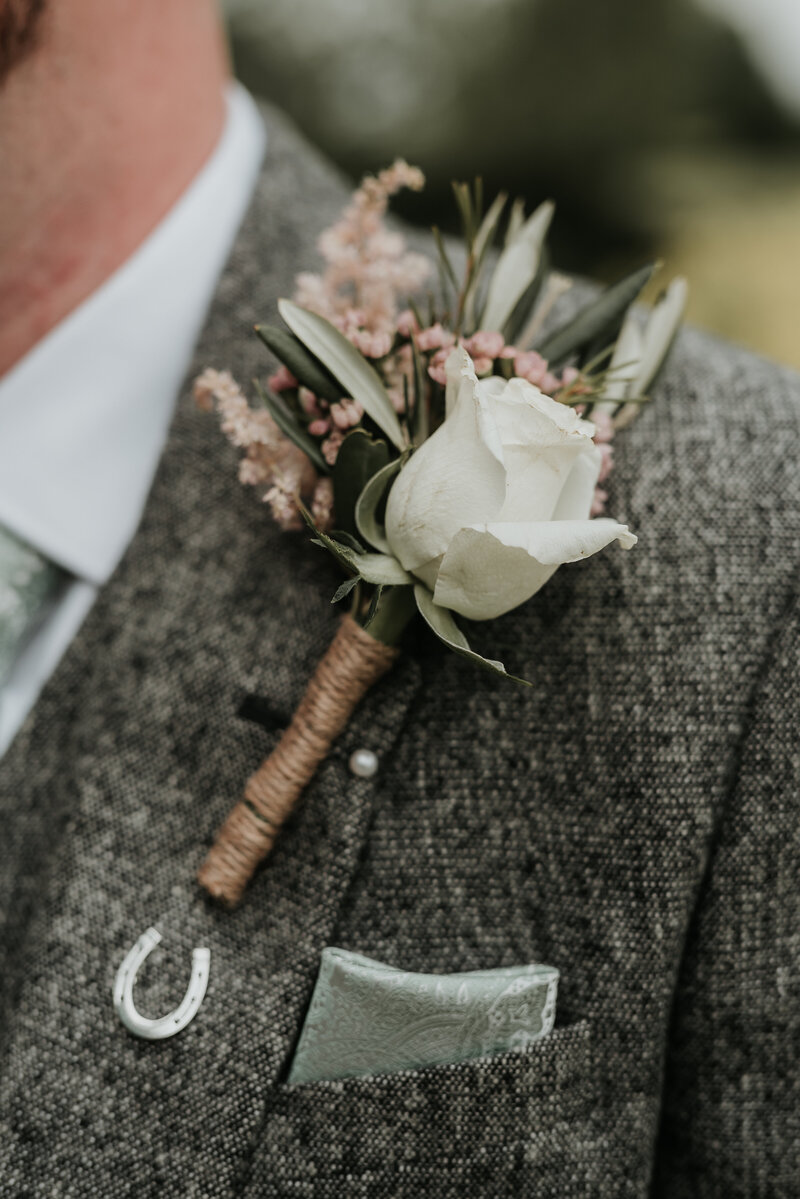 Spring wedding buttonhole with cream rose on grey tweed jacket