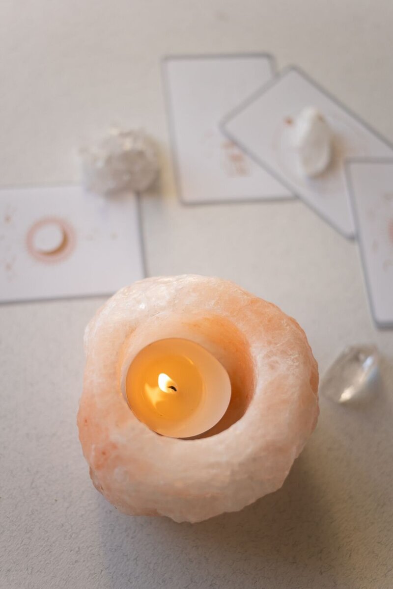 Lit candle in a pink Himalayan salt holder surrounded by crystals and oracle cards, symbolizing spiritual reflection and clarity