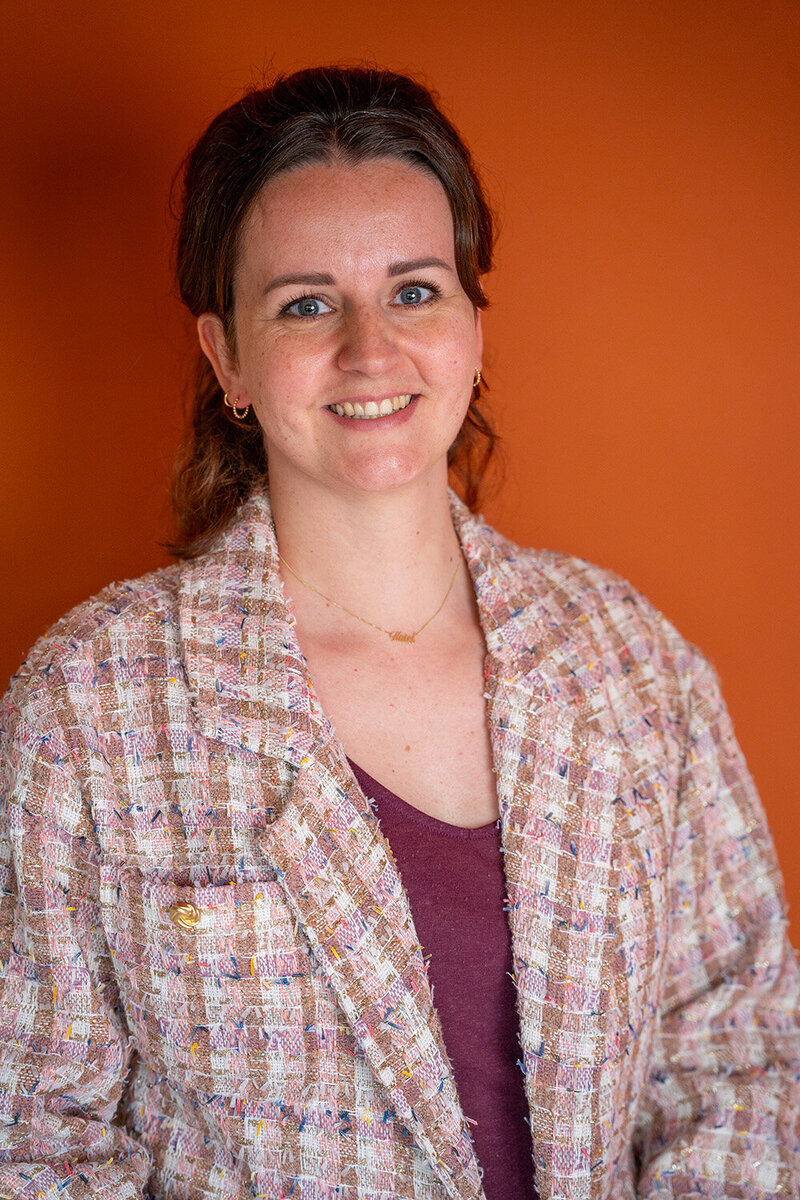 Portret van interieurstylist met warme oranje achtergrond en stijlvolle blazer