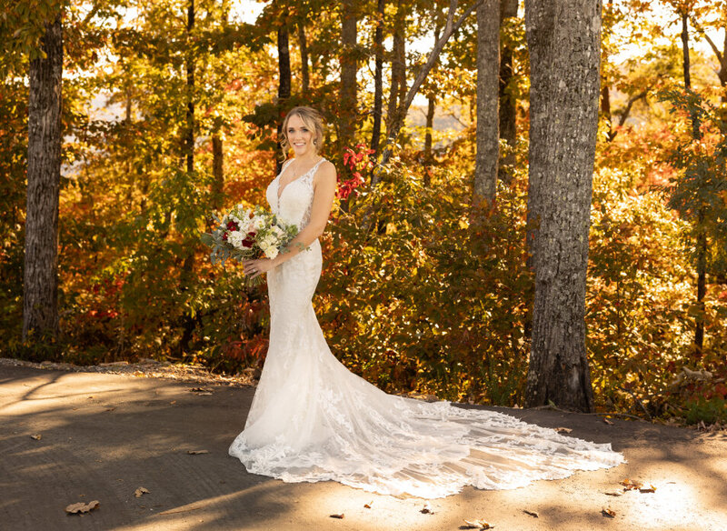 A bride poses and smiles with the trees behind her.